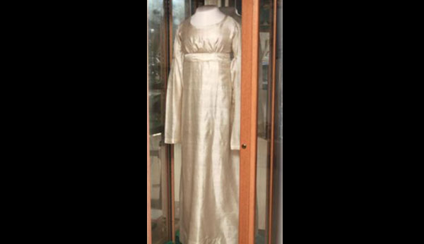 Vintage off-white, full-length dress in a glass case.