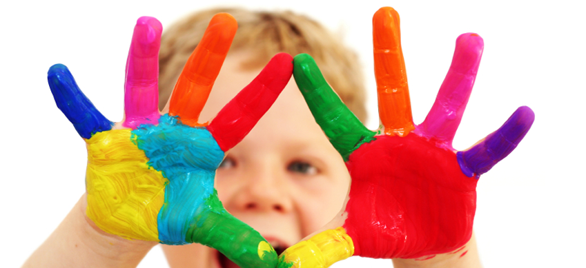 A young boy holds his hands up which are brightly painted with many colors.