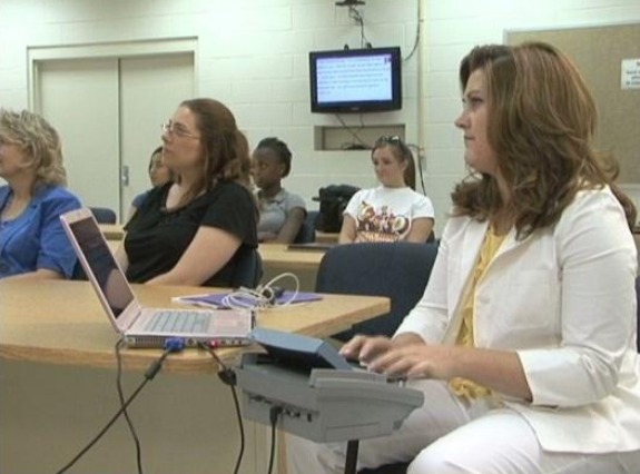A woman types on a CART device in a room with other people sitting.