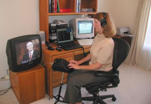 A woman sits in front of a TV, wearing headphones and typing.