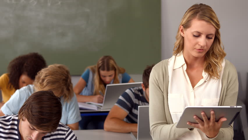 A teacher in a classroom uses a computer tablet.
