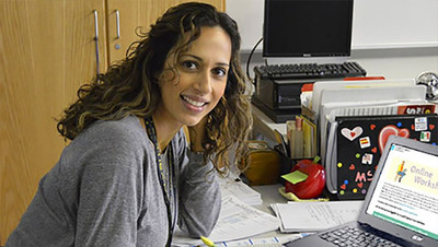 A young woman smiles towards the camera while sitting in front of an open laptop