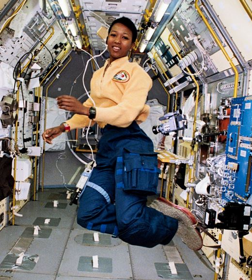 Mae Jemison floating inside a small room with numerous wires and electronics.